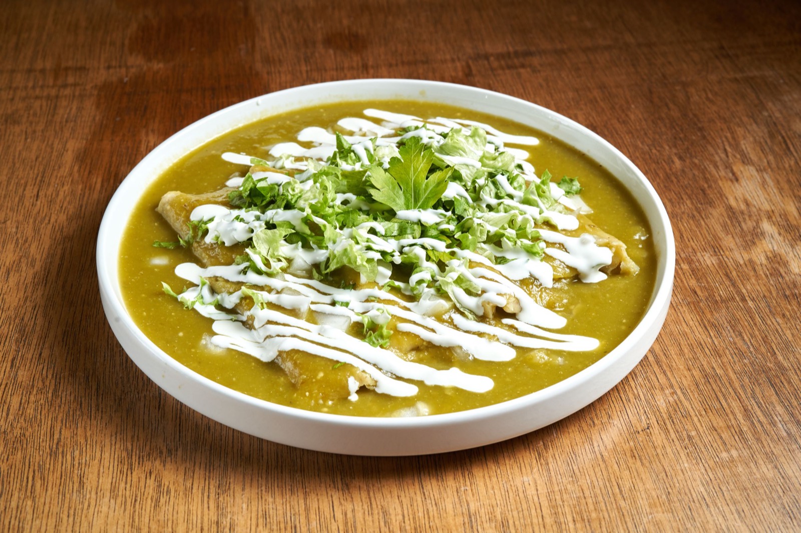 Un plato de enchiladas verdes con crema, cebolla y cilantro sobre una mesa de madera.