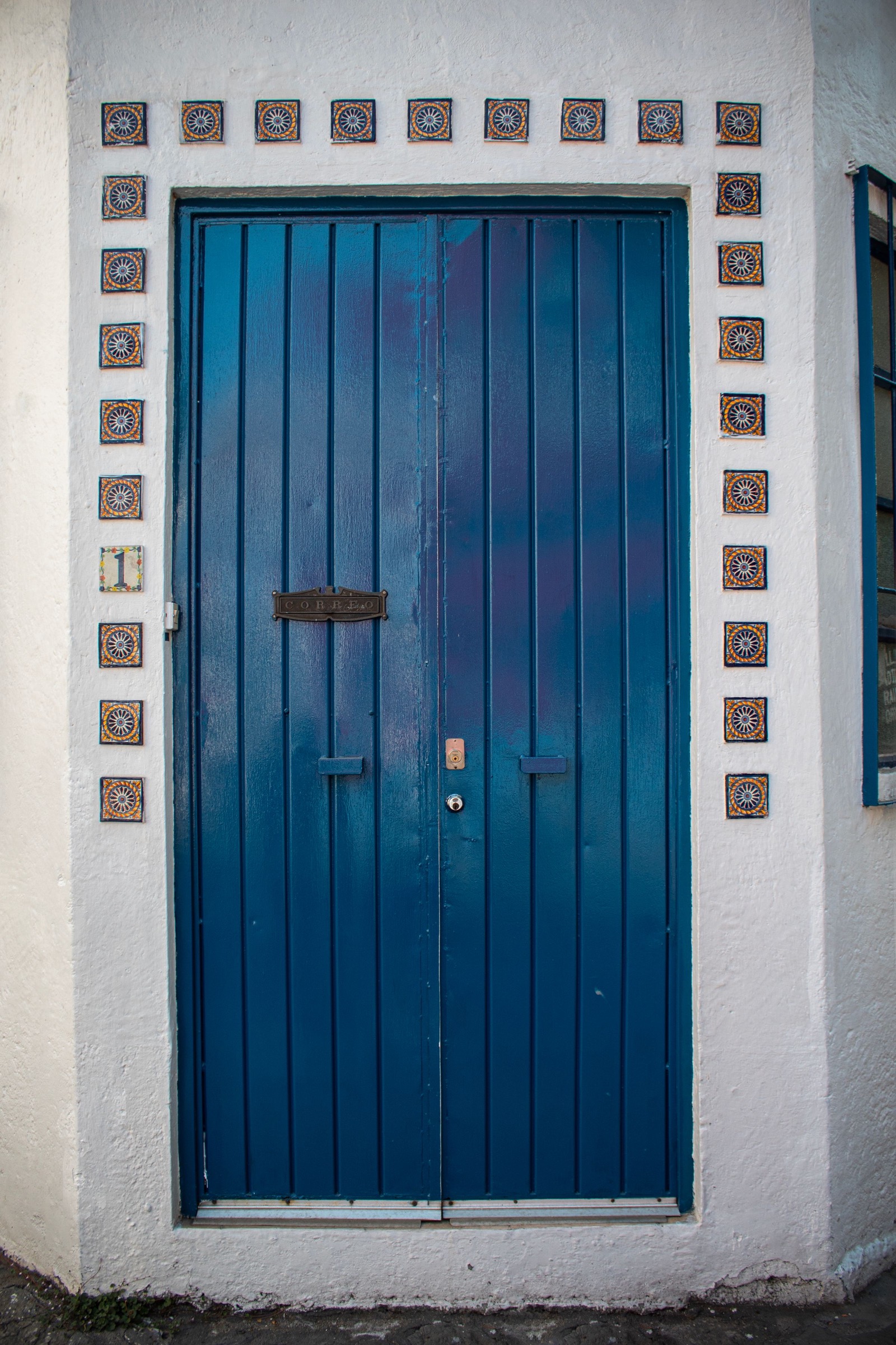 Una puerta de madera azul en un muro blanco, enmarcada por azulejos pintados.